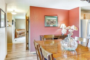 A dining area with a wooden table, chairs, a vase with flowers, and a framed picture on the wall.