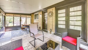 Ein überdachter Patio-Bereich mit Korbmöbeln, einer Uhr an der Wand und einer Tür mit Fensterfeldern.