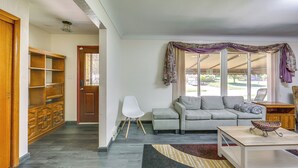 Ein Wohnzimmer mit grauem Sofa, einem weißen Sessel, einem Holzschrank und einem Tisch mit einer gewebten Schale.