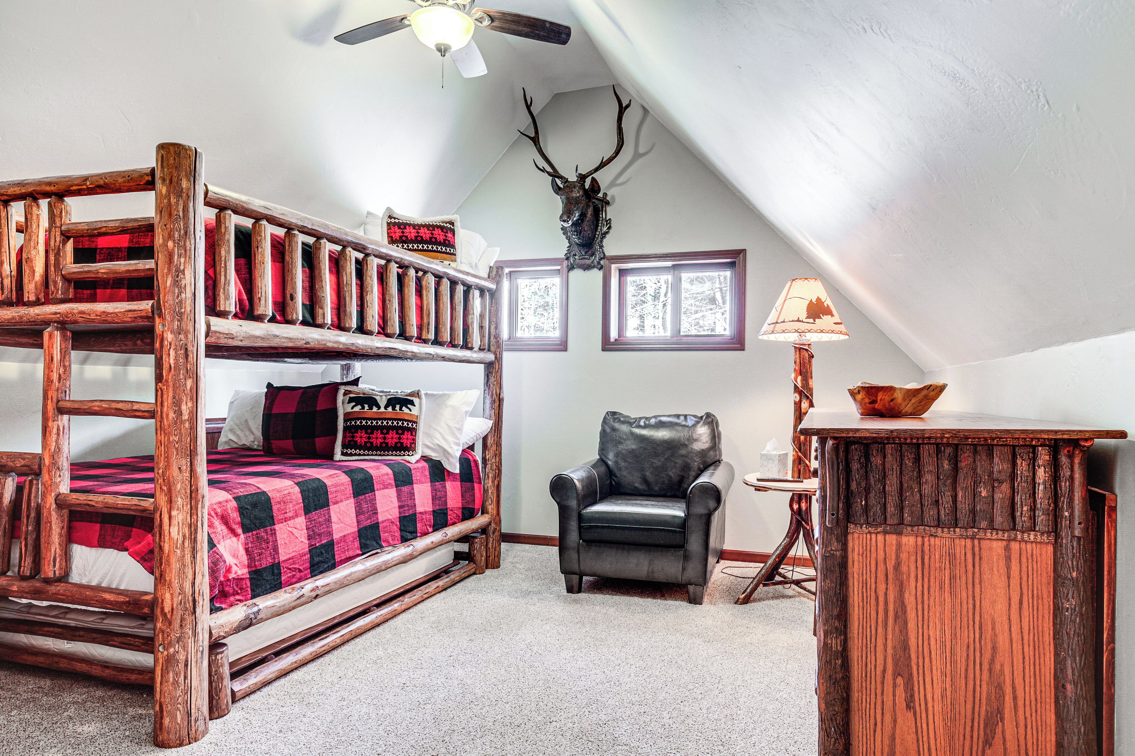 A room with a bunk bed, a desk with a lamp, a chair, and a deer head on the wall.