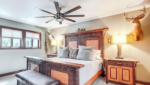 A bedroom with a large bed, a wooden bench, a ceiling fan, a mounted deer head, and a nightstand with a lamp. - 'northwood Tours Escape': Hot Tub & Lake Access! (Minocqua)