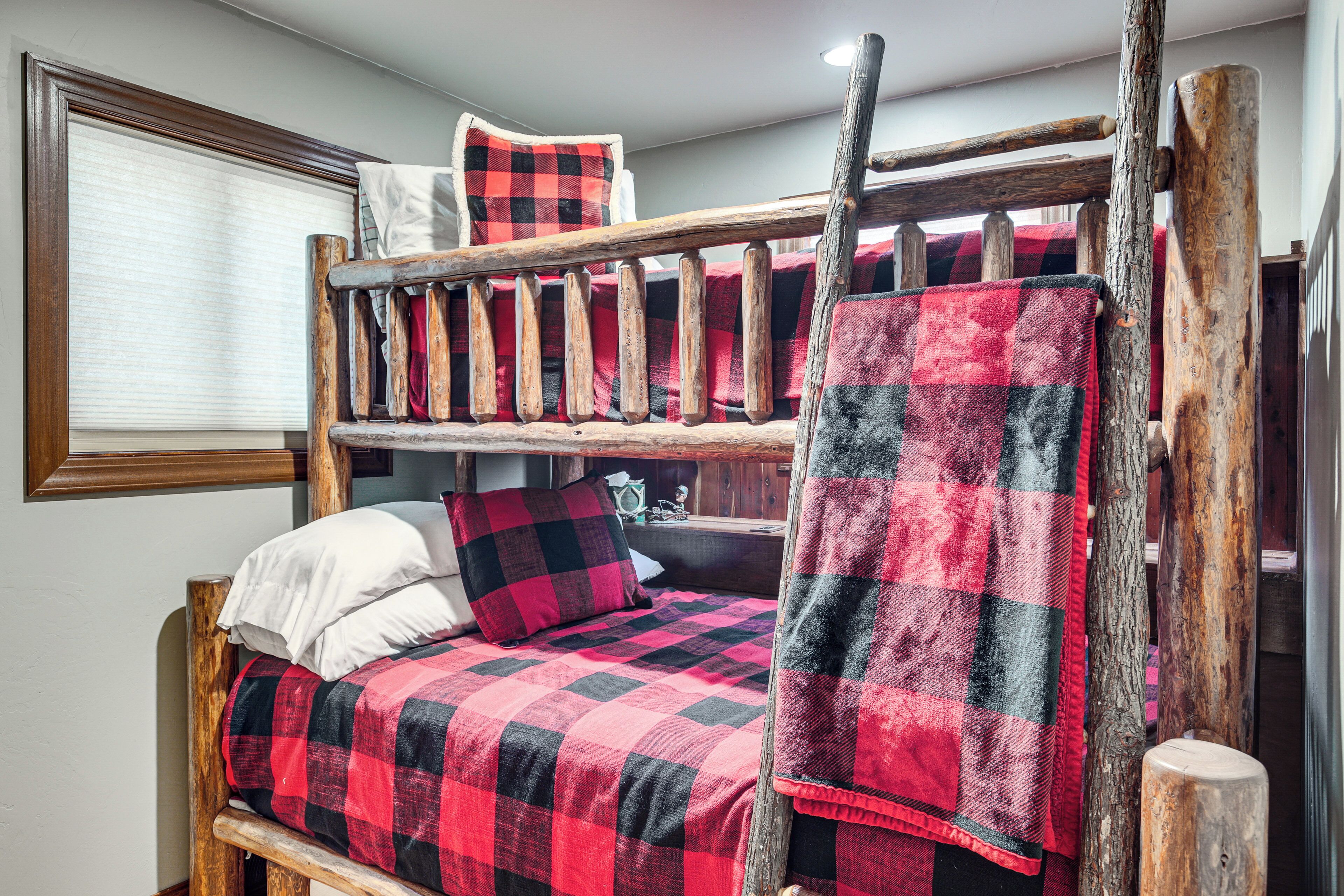 A bunk bed with a red and black checkered bedspread, wooden headboard, and a ladder.