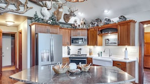 A kitchen with wooden cabinets, a large island with a marble countertop, and a ceiling adorned with mounted animal heads. - 'northwood Tours Escape': Hot Tub & Lake Access! (Minocqua)