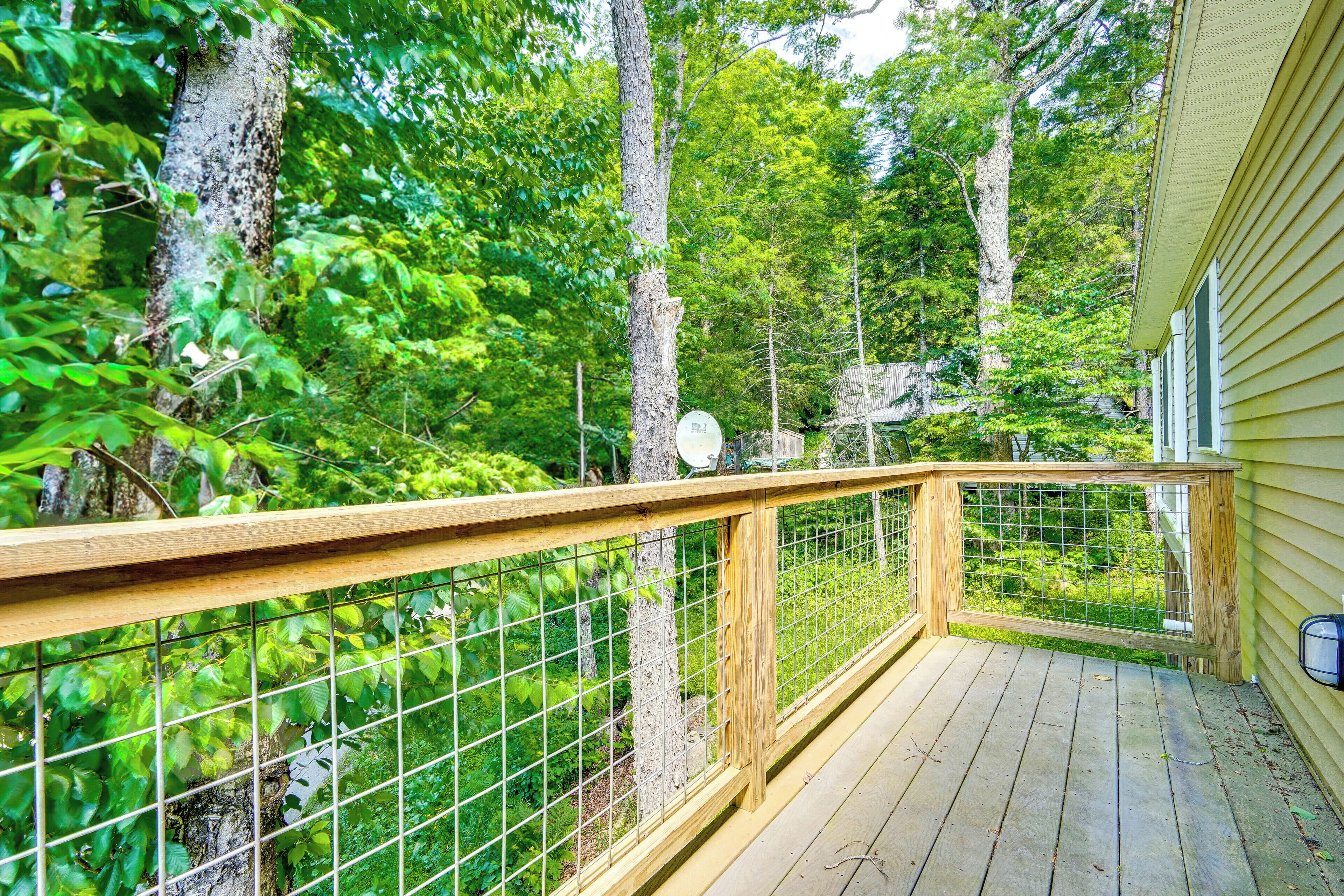 Une terrasse en bois avec une rambarde en métal, donnant sur une zone boisée.