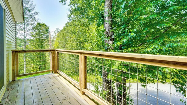 Une terrasse en bois avec une rambarde en métal donnant sur une zone boisée.