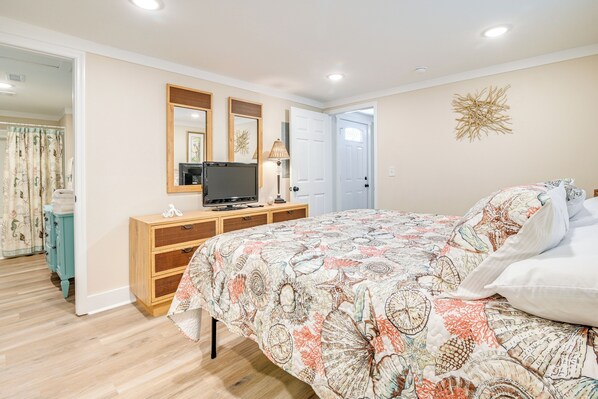 Une chambre à coucher avec un lit, une commode, un téléviseur et une porte.