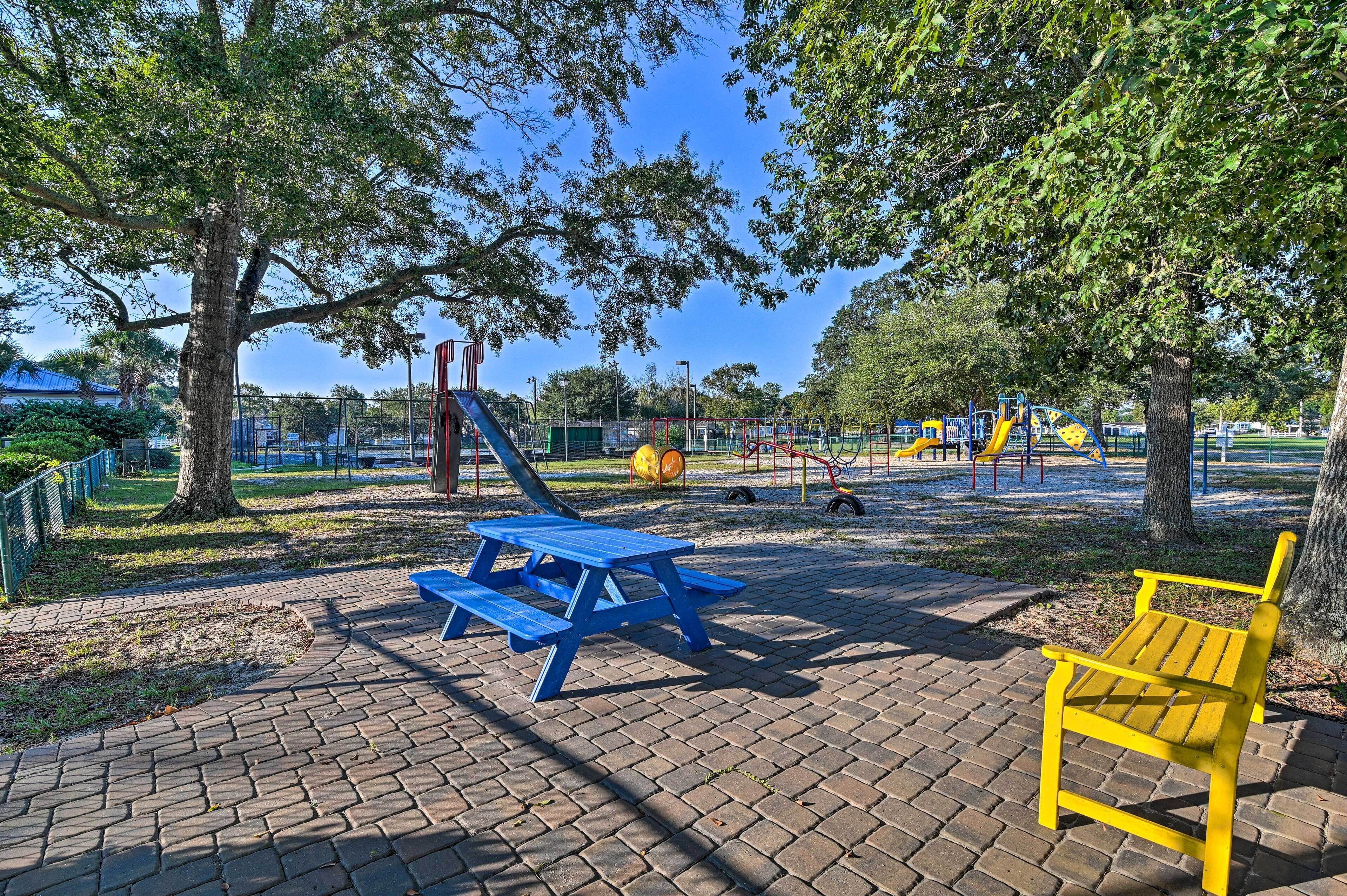A park with a blue picnic table, a yellow bench, and playground equipment.