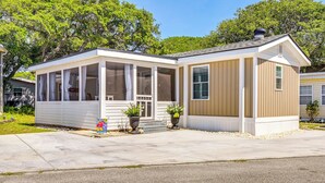 A single-story mobile home with a covered porch, a small front yard, and a clear sky. - Walk to Ocean: Myrtle Beach Home w/ Screened Porch (Murrells Inlet)