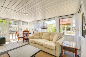 A sunlit room with a beige sofa, wooden chairs, and a glass coffee table. - Walk to Ocean: Myrtle Beach Home w/ Screened Porch (Murrells Inlet)