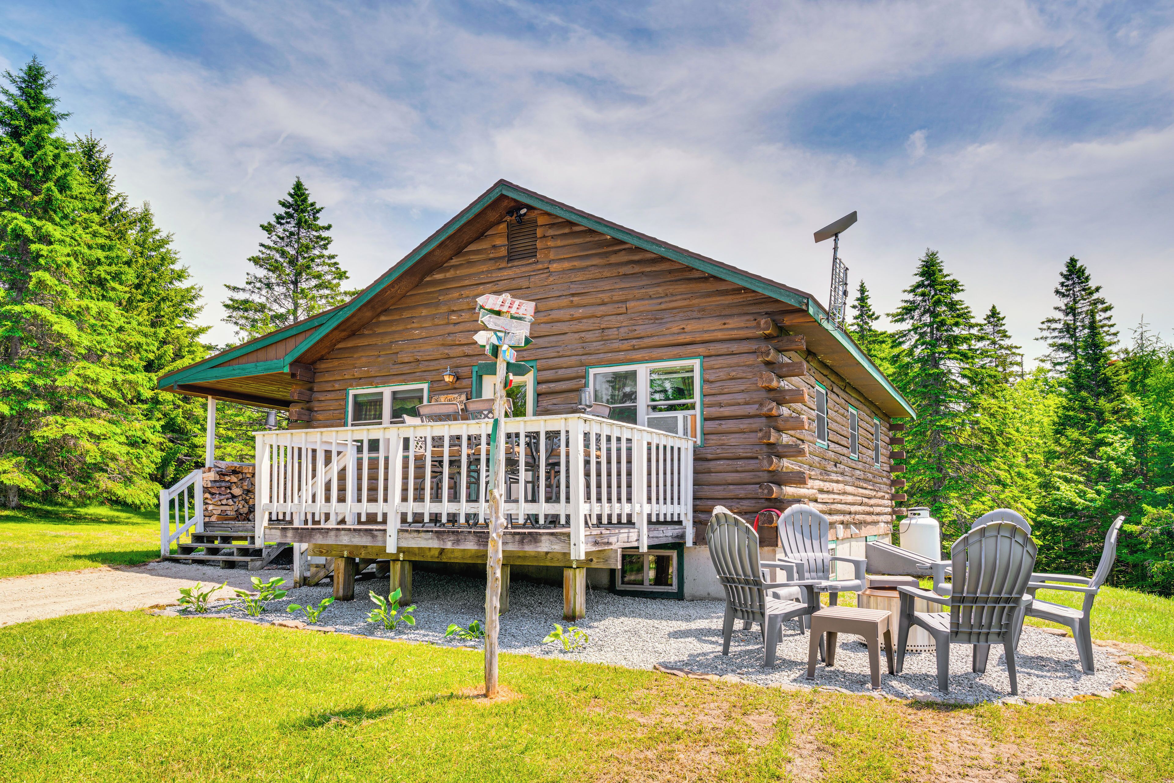 A log cabin with a deck, outdoor seating, and a gravel path leading to the entrance.