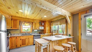 A wooden cabin kitchen with a central island, bar stools, and a refrigerator. - Rustic Cabin in West Danville w/ Deck & Fire Pit! (West Danville)