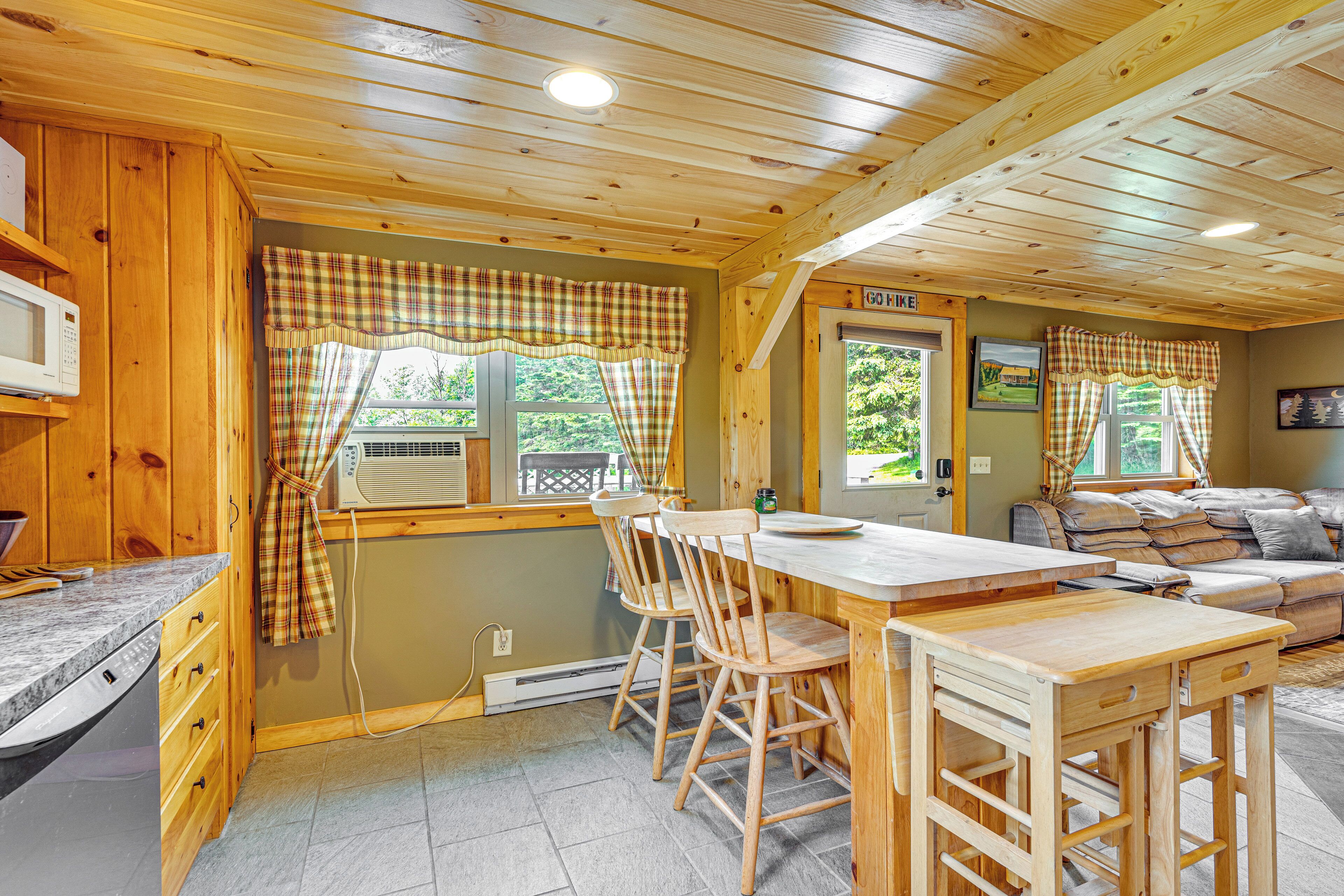Interior de una cabaña de madera con una zona de cocina que incluye una mesa y sillas de madera, un microondas y un sofá en la sala de estar.