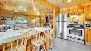 A wooden cabin interior with a kitchen area featuring a refrigerator, stove, and dining space with a table and chairs. - Rustic Cabin in West Danville w/ Deck & Fire Pit! (West Danville)