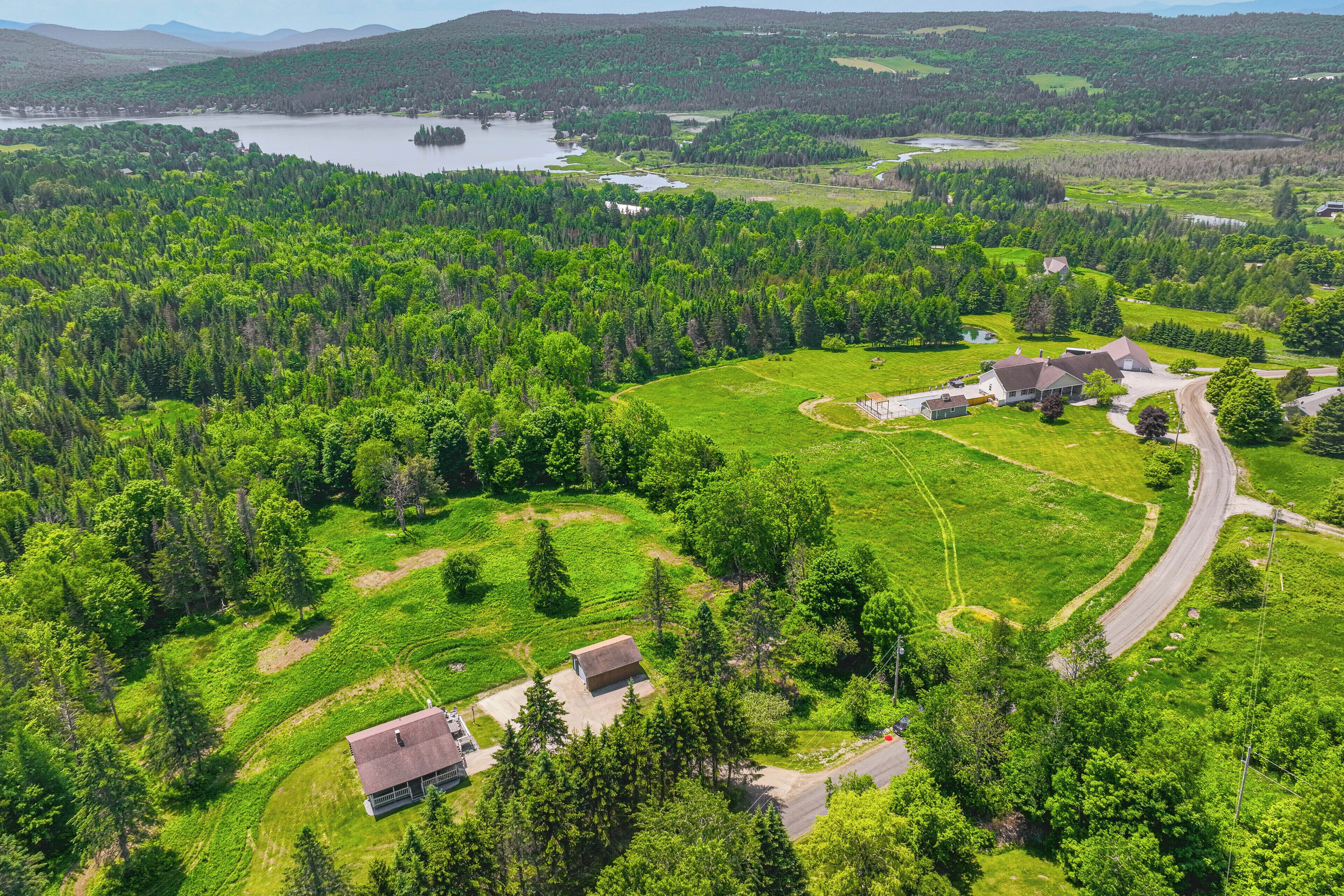 Une vue aérienne d’une zone rurale, avec une grande maison entourée d’une végétation luxuriante et d’un lac.