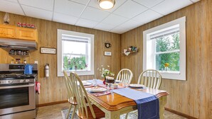 A dining area with a wooden table, chairs, and a kitchen area with a stove and cabinets. - Charming Stone Cottage in Marion w/ Fire Pit! (Marion)