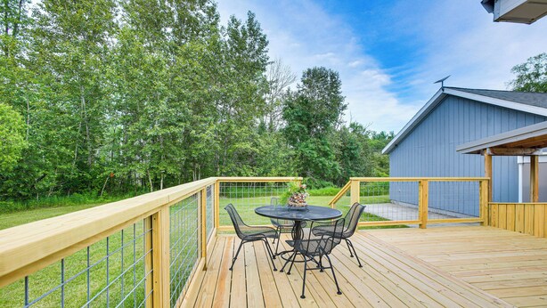 A wooden deck with a round table and chairs, surrounded by a metal fence and trees. - Charming Stone Cottage in Marion w/ Fire Pit! (Marion)