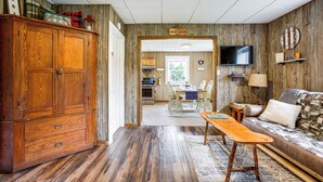 A wooden-finished living room with a sofa, a wooden coffee table, and a television mounted on the wall. - Charming Stone Cottage in Marion w/ Fire Pit! (Marion)