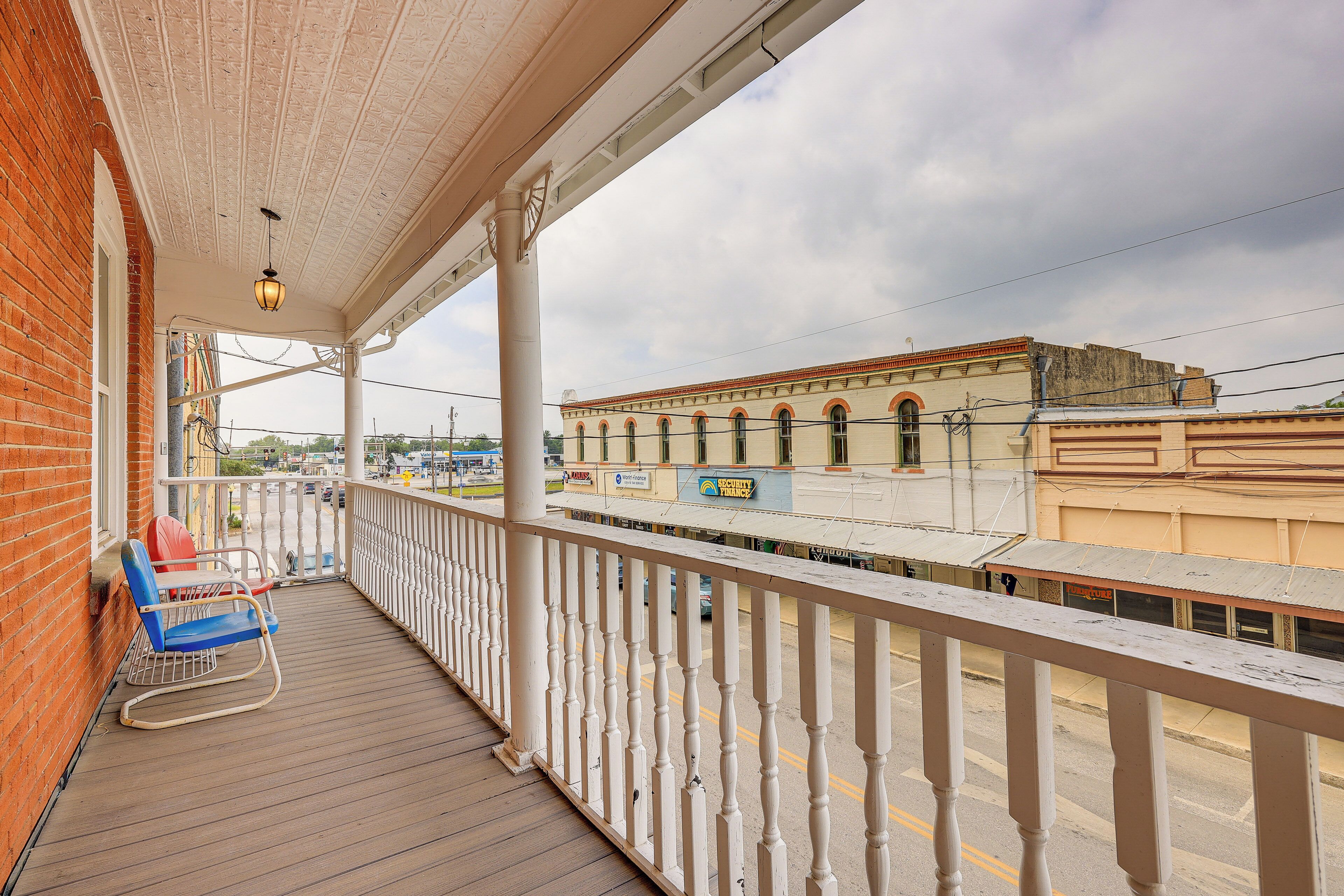 A covered balcony with a white railing, a blue rocking chair, and a brick wall.