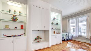 A room with white cabinets, glass shelves, and a wooden floor.