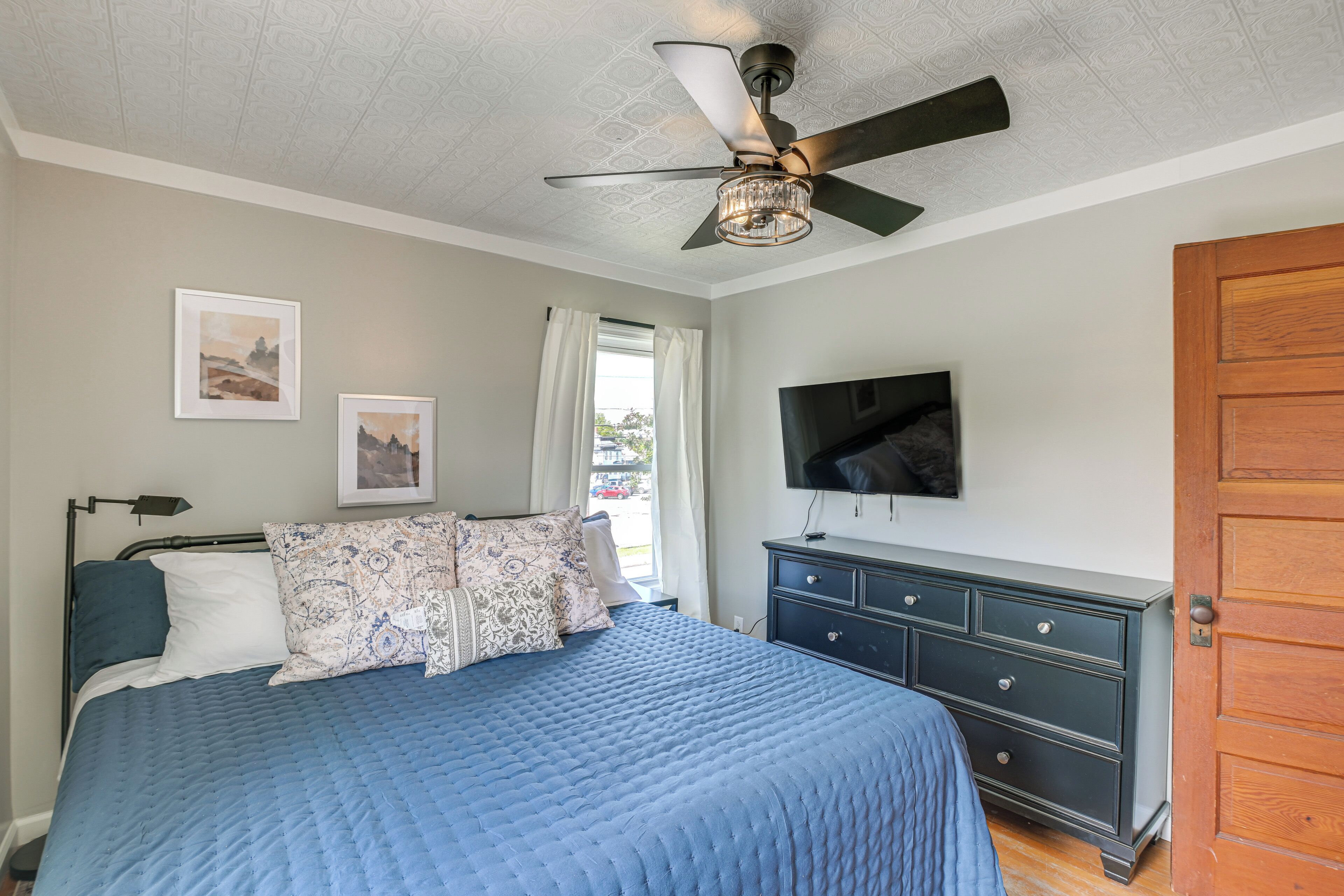 Une chambre à coucher avec un lit, une commode, un ventilateur de plafond et un téléviseur fixé au mur.
