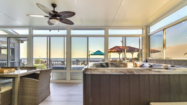 A spacious balcony with a hot tub, wicker furniture, and a view of the ocean.