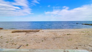 A sandy beach with a wooden fence in the foreground and a calm sea in the background.