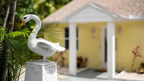 Une statue de cygne blanc, posée sur un piédestal devant un bâtiment jaune surmonté d’un toit blanc.