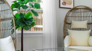 Une chaise en osier avec des coussins, une table en verre et une plante en pot, le tout dans une pièce lumineuse dotée d’une fenêtre.