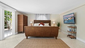 Une chambre dotée d'un grand lit, d'une télévision, d'une armoire en osier et d'une porte-fenêtre coulissante donnant sur un balcon.