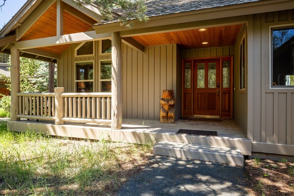 A wooden porch with a bench, a front door with glass panels, and a small step leading to the entrance.
