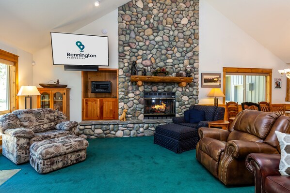 Una sala de estar acogedora con chimenea de piedra, sofás de cuero y un televisor montado en la pared.