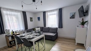 A modern living room with a dining area, a sofa, a TV, and a small plant. - Haus Im Hochtal - upstairs, 2 bedrooms apartment - small room with 2 single beds (Bad Bleiberg)