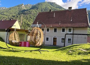 Une maison avec un toit recouvert de tuiles rouges, de nombreuses fenêtres et une porte. On aperçoit un fauteuil suspendu au premier plan.