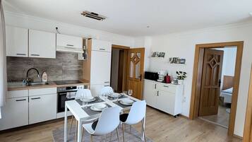 A modern kitchen with white cabinets, a dining area with a table and chairs, and a wooden floor.
