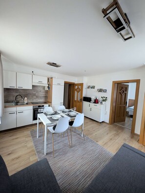 A modern kitchen with white cabinets, a dining area with a table and chairs, and a wooden floor.