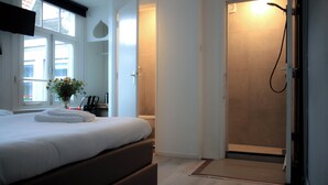 Quarto de hotel com cama, chuveiro e janela com vista.