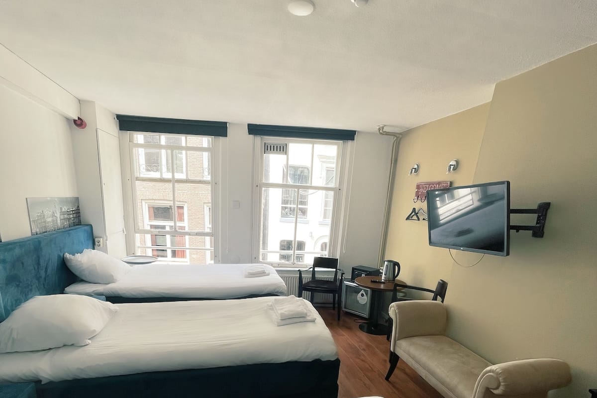Et hotelværelse med to senge, et skrivebord, en stol og et fjernsyn ophængt på væggen.
