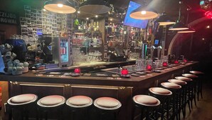 Uma área de bar com um balcão comprido, vários bancos e um letreiro da Heineken.