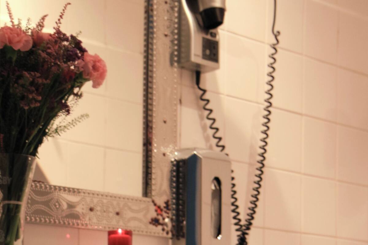 Et badeværelse med håndvask, spejl, hårtørrer og en vase med blomster.
