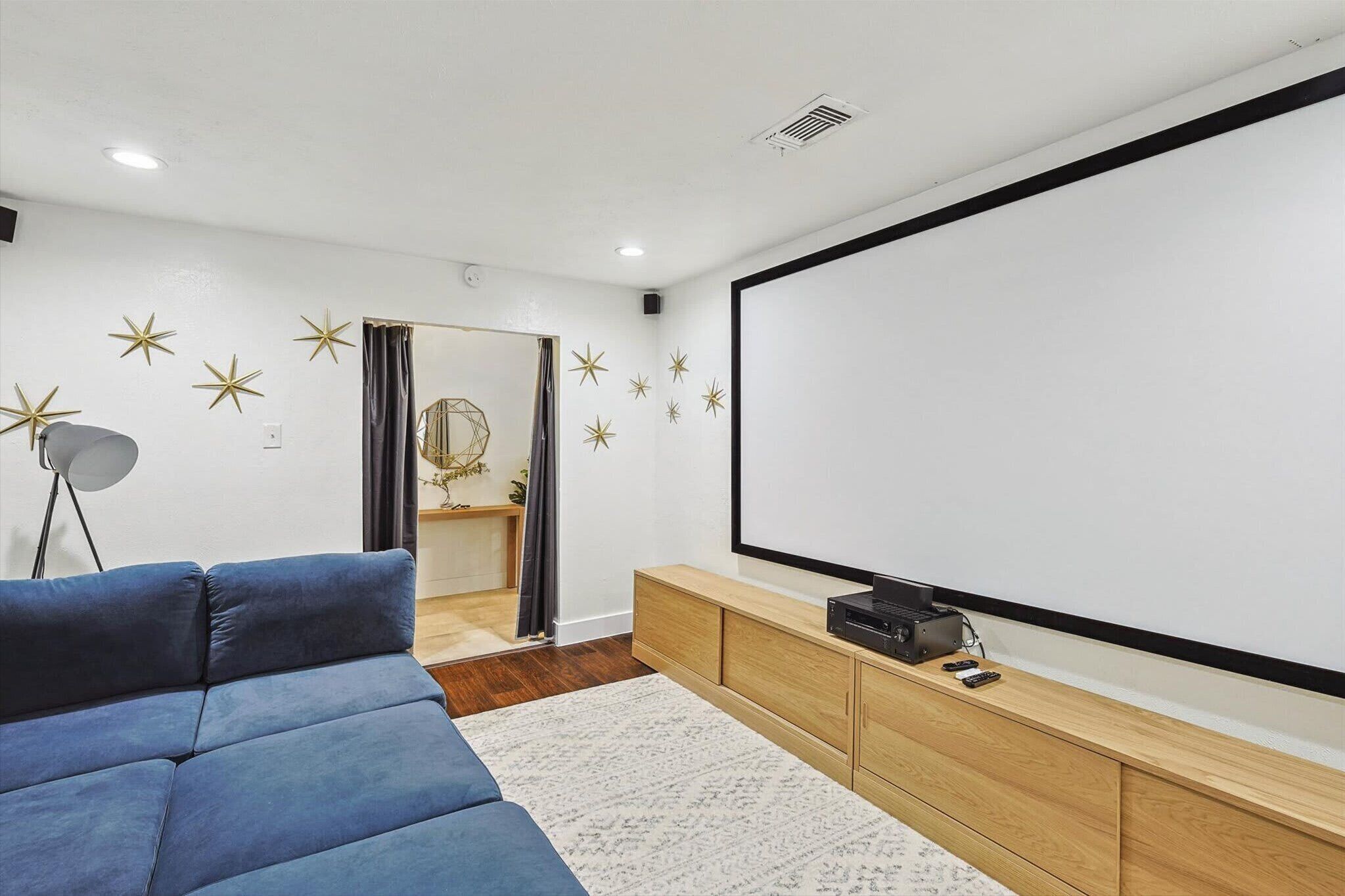 A modern living room with a large flat-screen TV, a blue sofa, a wooden entertainment unit, and decorative star wall decals.