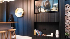 Ein modernes Wohnzimmer mit an der Wand befestigtem Fernseher, einem runden Spiegel und einem Bücherregal mit Büchern und Dekoration.