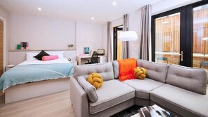 Ein modernes Hotelzimmer mit einem Bett, einem grauen Sofa, einem Schreibtisch und einem Fenster mit Vorhängen.