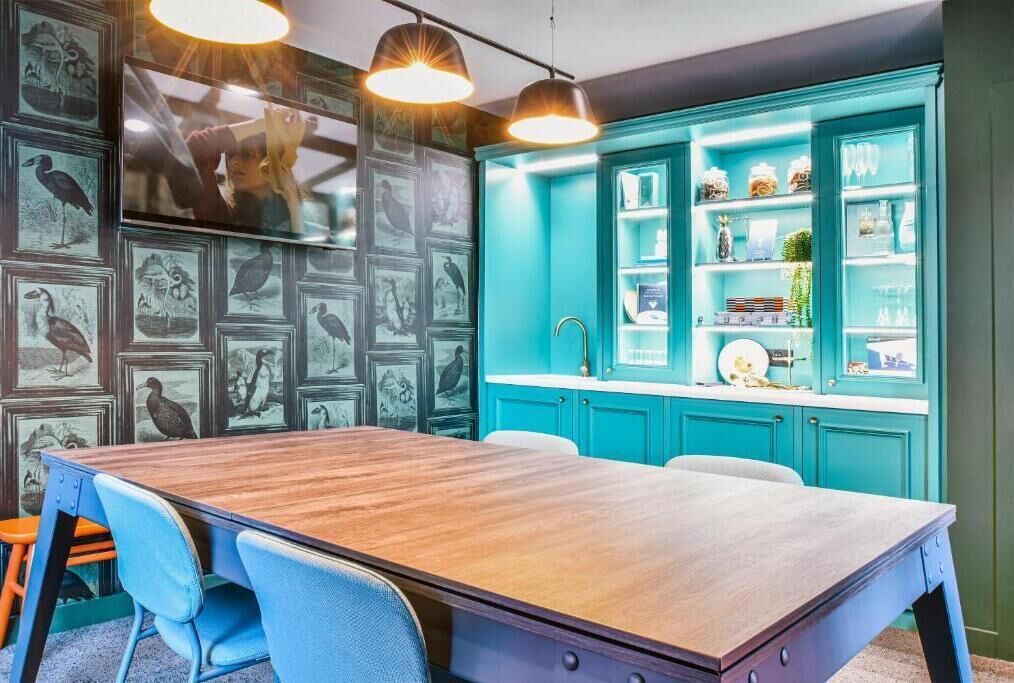 Un salón de conferencias con una mesa de madera, sillas azules y armarios color turquesa con estanterías.