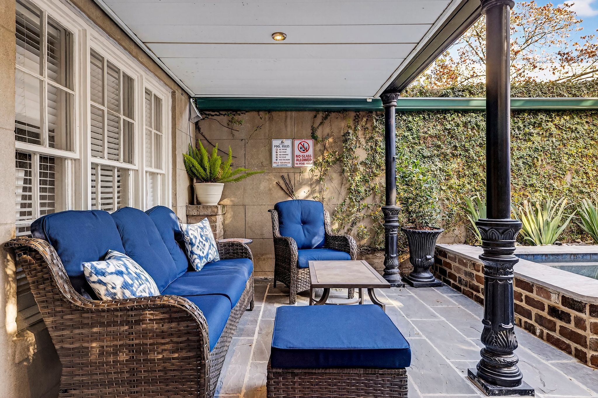 A covered patio area with wicker furniture, a small table, and a sign indicating no glass allowed.