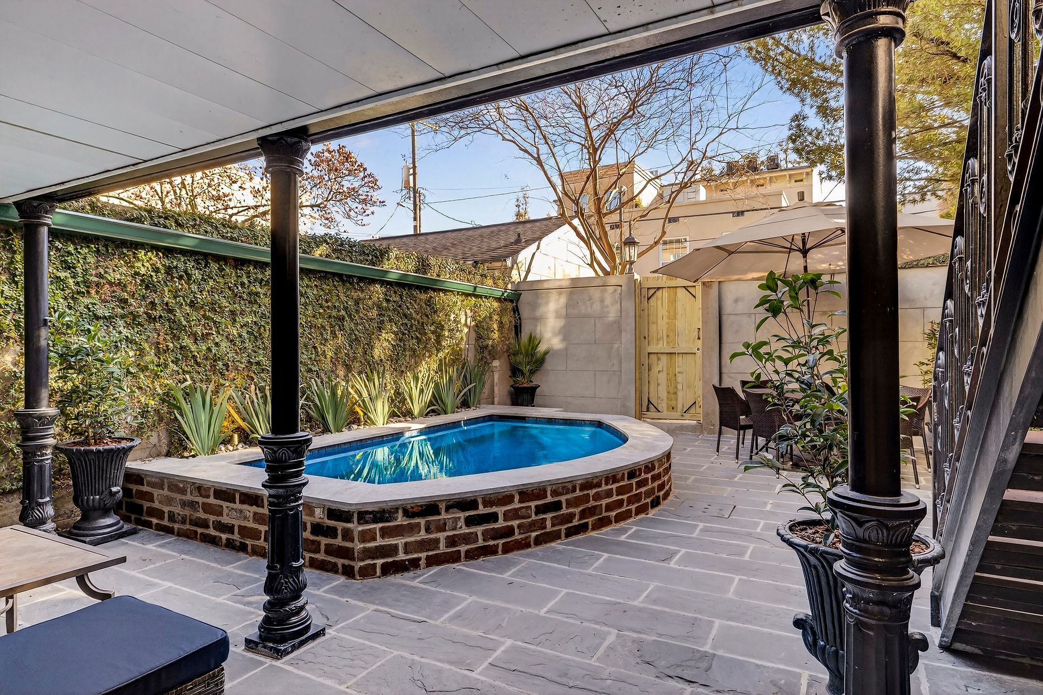 Un patio couvert avec une piscine, un sol en briques et du mobilier d’extérieur.