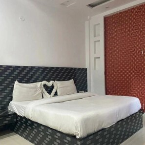 A modern hotel room with a bed featuring a geometric-patterned headboard, a heart-shaped pillow arrangement, and a red patterned wall.