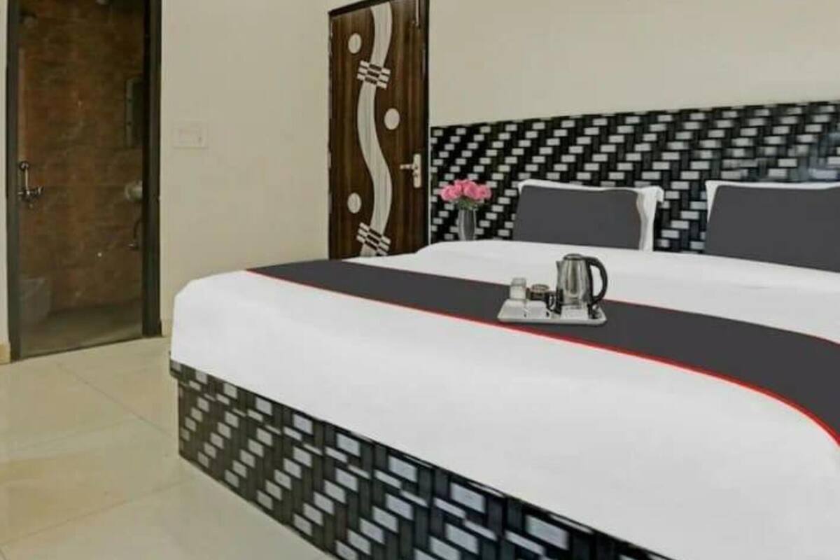 A hotel room with a bed, a bedside table with a kettle, and a door with a unique design.