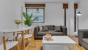 A modern living room with a grey sofa, white coffee table, and a dining area with a white table and wooden chairs. - Queens Quay Mansion House Flat (London)