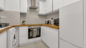 A modern kitchen with white cabinets, a built-in oven, a washing machine, and a wooden countertop. - Queens Quay Mansion House Flat (London)