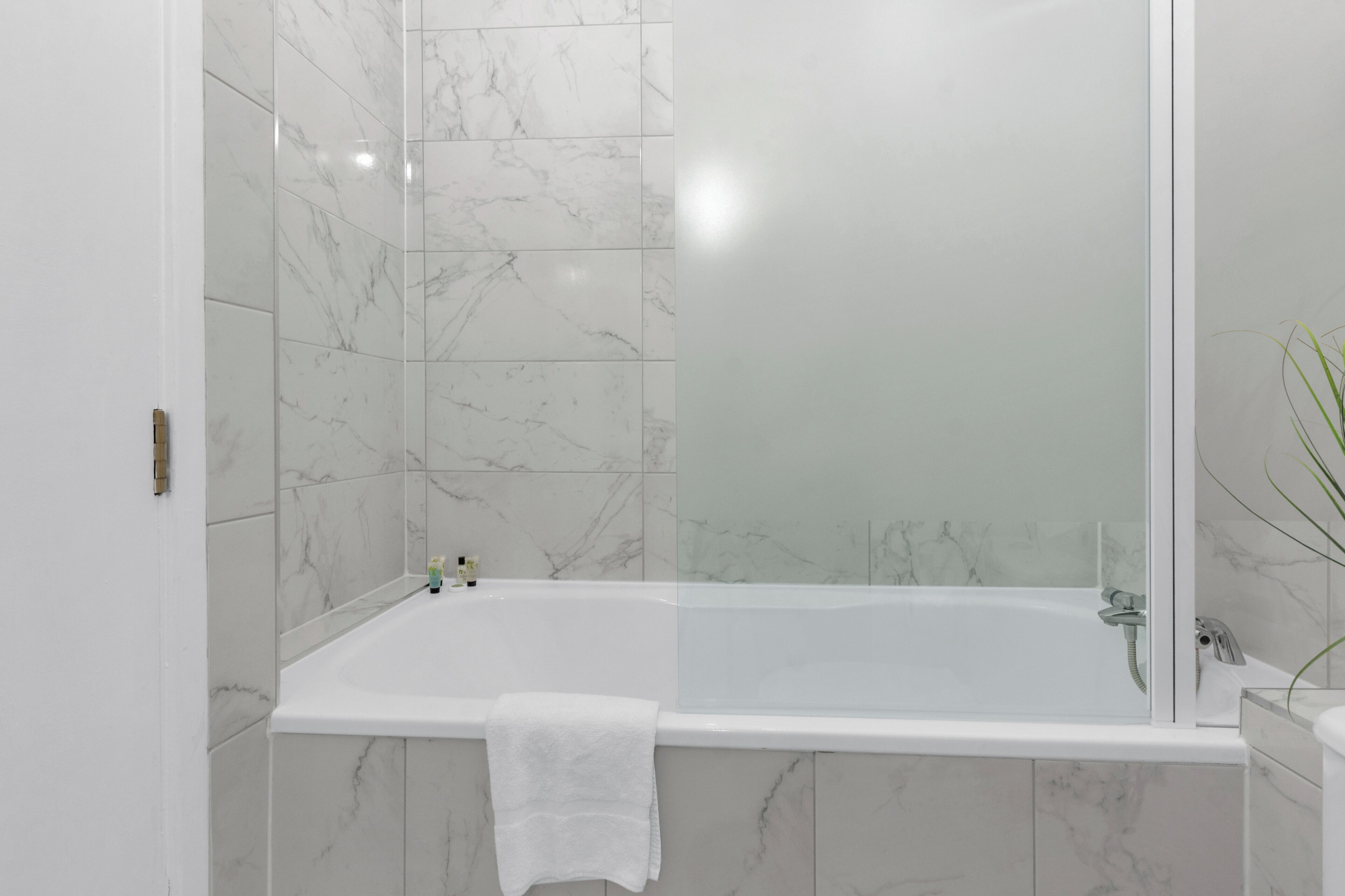 Un baño moderno con ducha de vidrio, bañera blanca y azulejos de mármol.